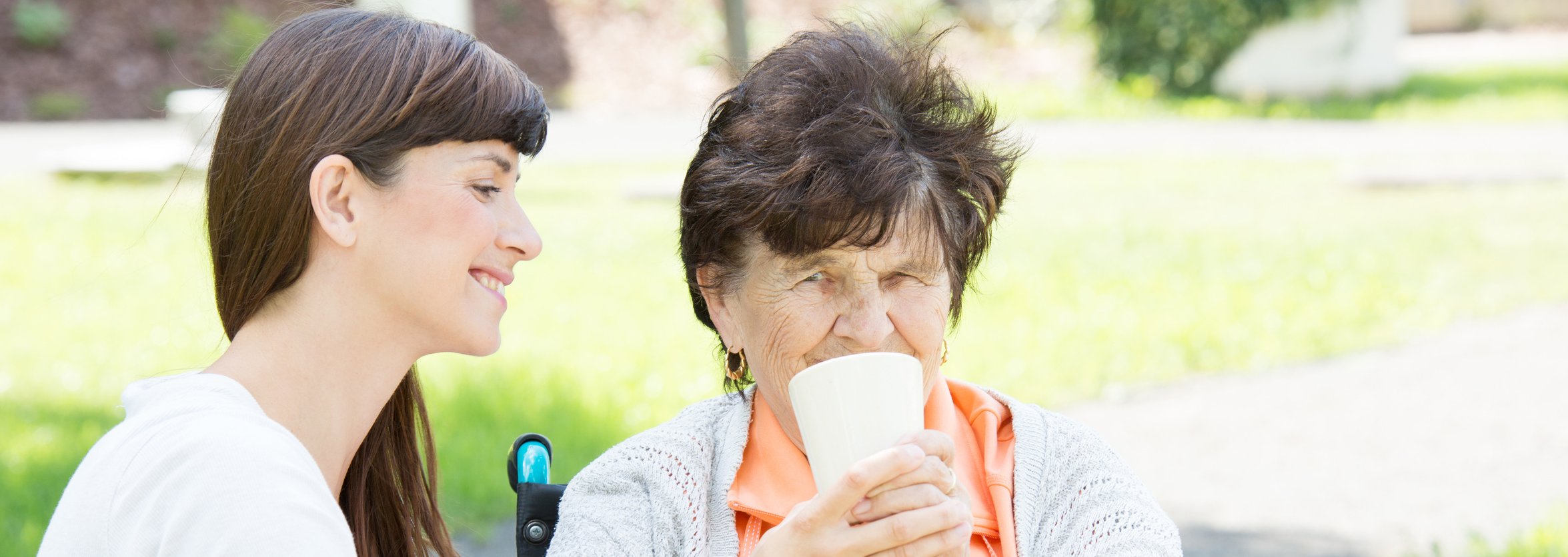 Junge Frau hilft älterer Dame im Rollstuhl beim Trinken