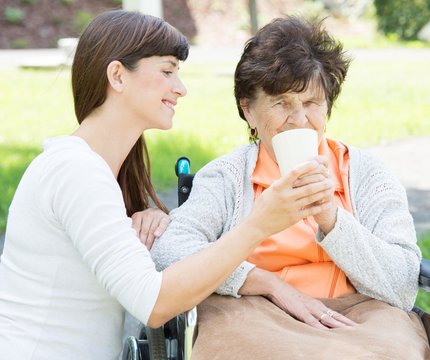 Junge Frau hilft älterer Dame im Rollstuhl beim Trinken