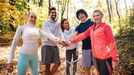Fünf sportlich gekleidete Menschen bilden im Wald eine Teamgeste