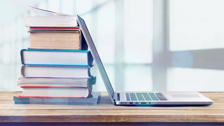 Aufgeklappter Laptop und Bücher stehen und liegen auf einem Tisch