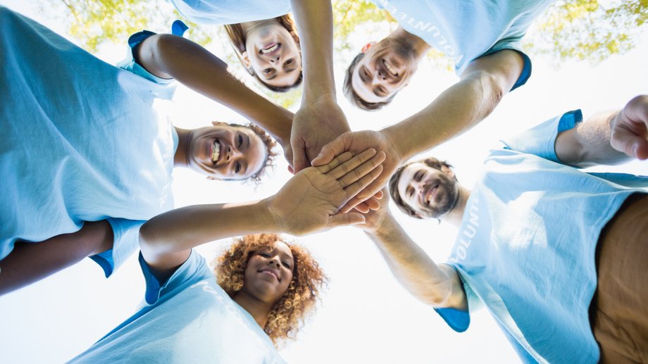 Fünf Menschen in blauen Shirts bilden mit ihren Händen eine Teamgeste