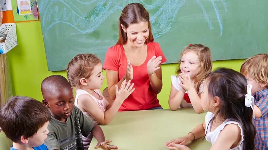 Erzieherin klatscht mit Kindern am Tisch