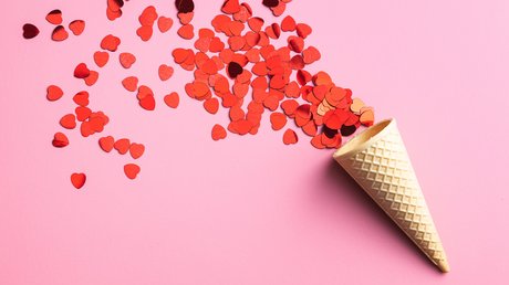 Aus einer Eistüte fliegen rote Papierherzchen