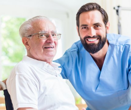 Junger Pfleger am UKR pflegt älteren Herren im Rollstuhl
